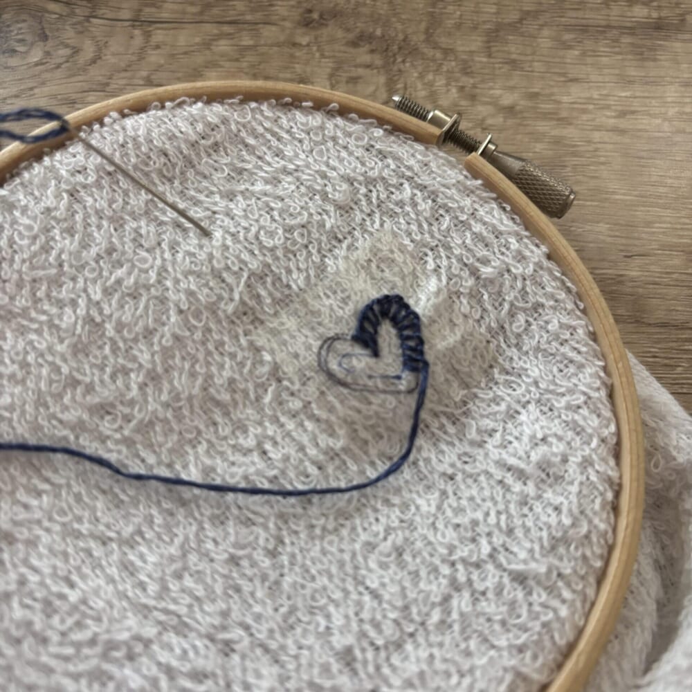 刺繍枠にはめられたフェイスタオルにハートを刺繍する様子