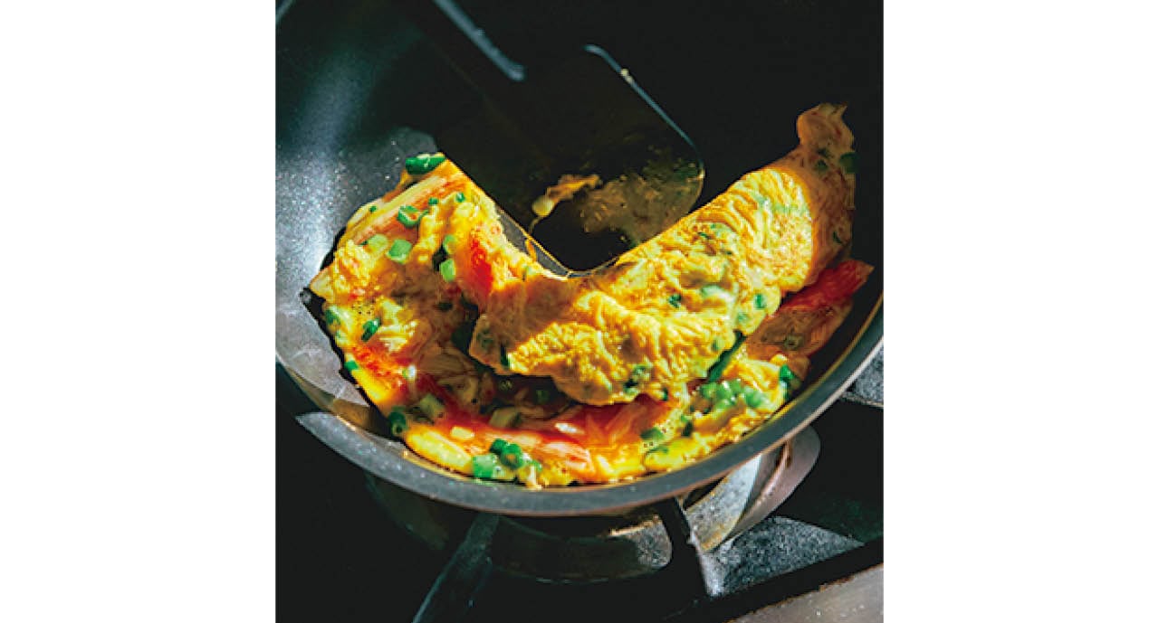 フライパンを斜めに傾け、へらを使って半分にたたむ。卵液が垂れないくらいまでしっかり焼く。