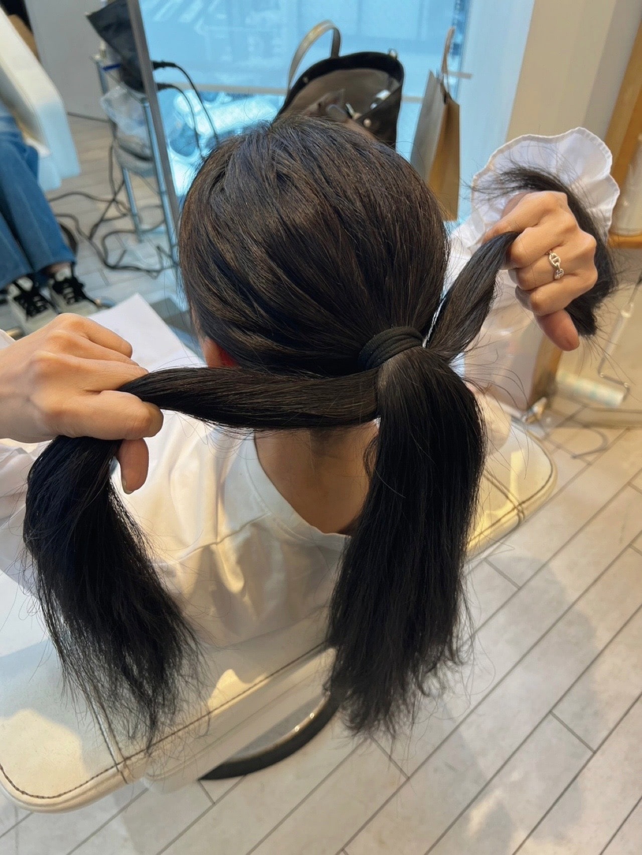 伊熊奈美さんひとつ結びアレンジのコツ③ 毛束を上側と下側に分け、根元の下側の髪だけを2つに裂くようにやや上向きに引っ張る。するとえり足のゆるみが引っ張り上がる。