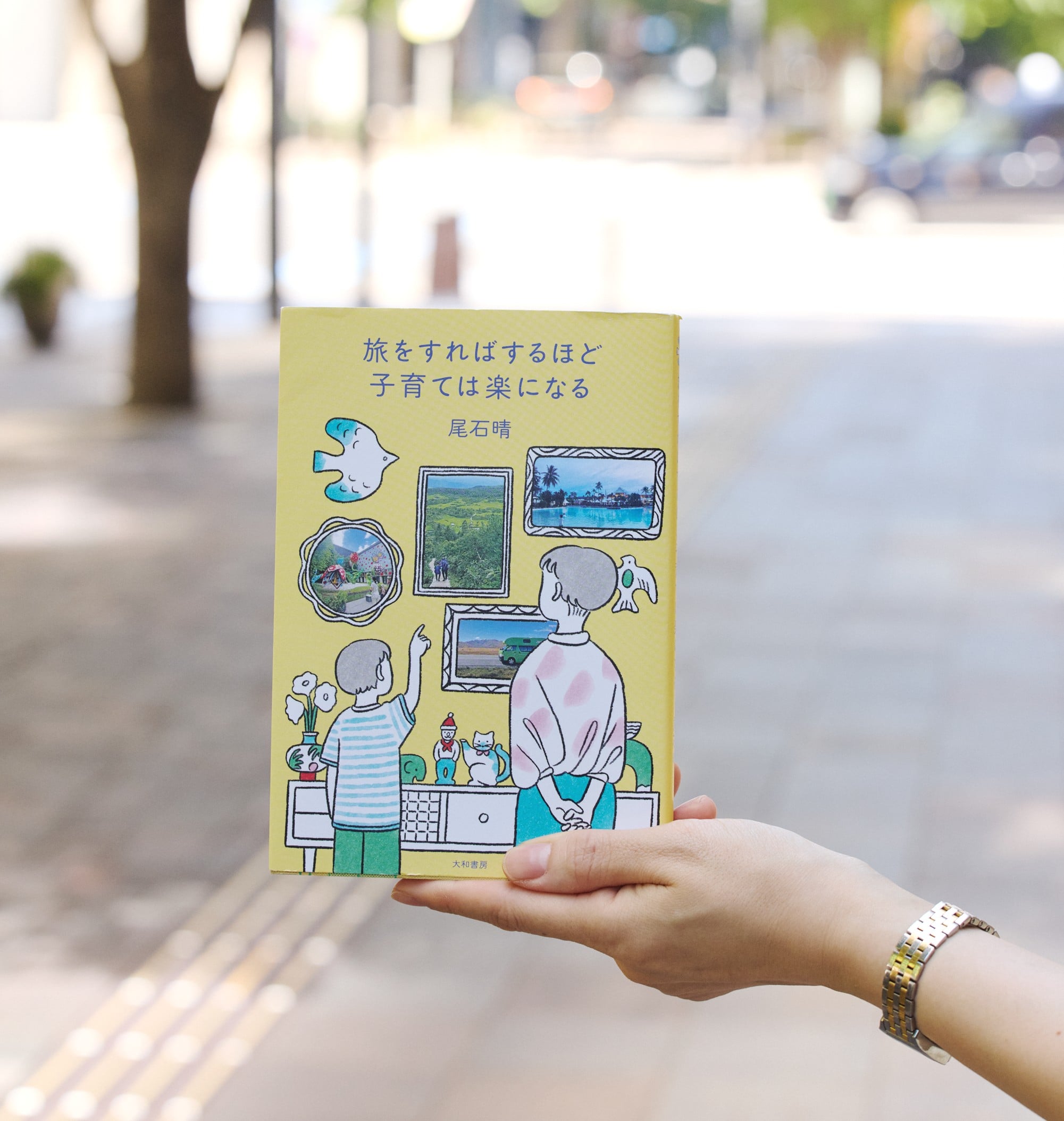 尾石晴さんの著書『旅をすればするほど子育ては楽になる』を手に持った写真