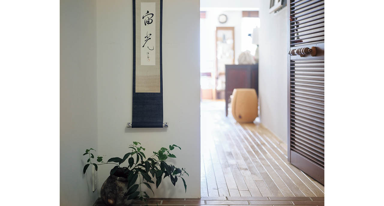 玄関を入って前面の壁に、春の光を意味する造語を。表装の布はシルクの藍染。