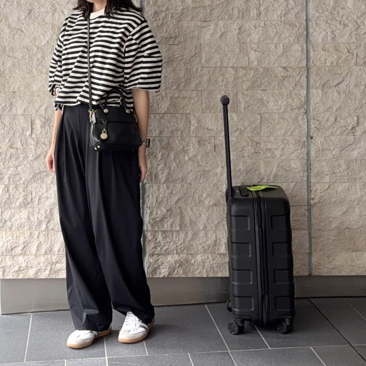 ユニクロの黒いワイドパンツ、アディダスのサンバ、FURLAの黒バッグ、無印良品の黒い20Lキャリーケースを合わせた韓国旅行コーデ