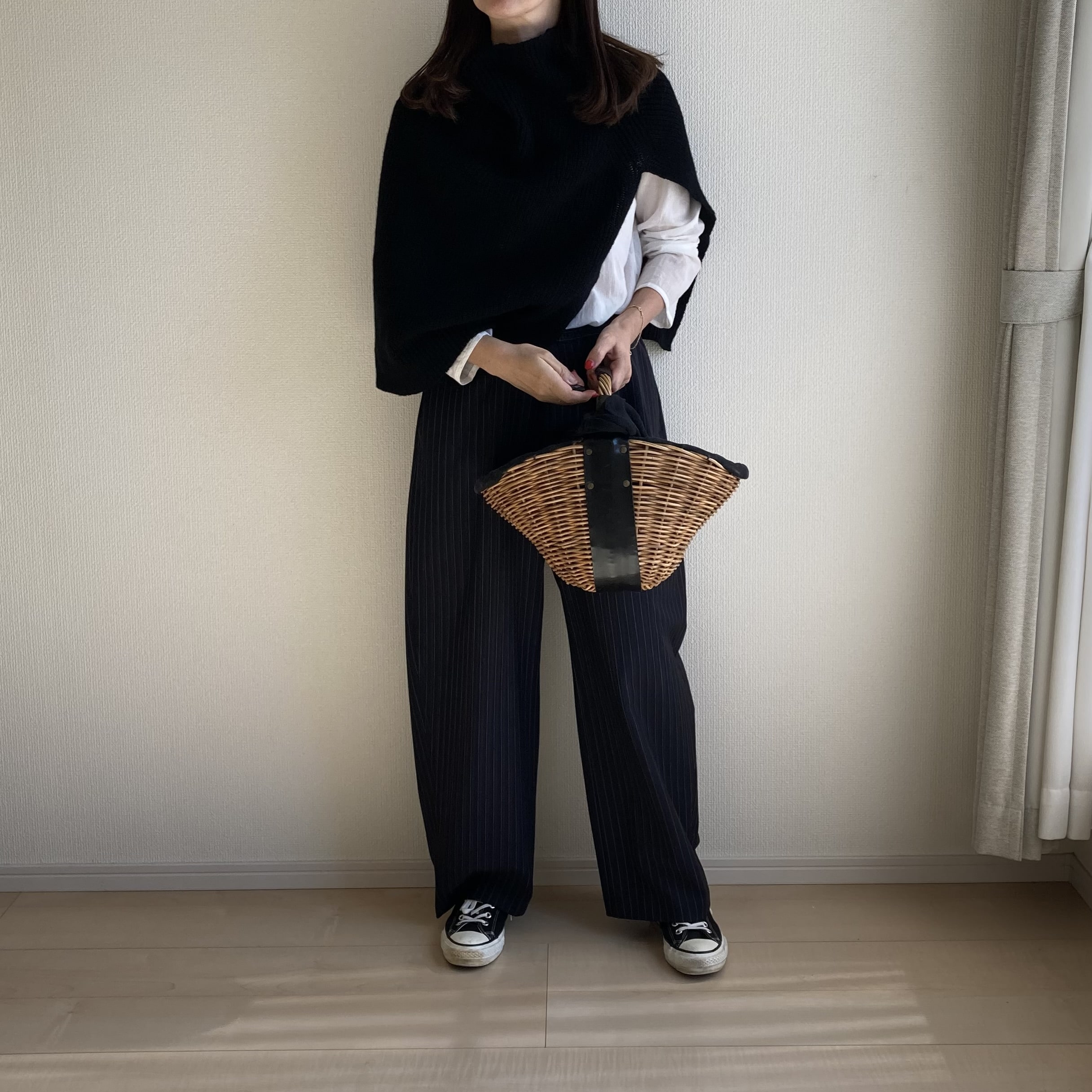 50代女性がツイードミルのニットポンチョを着用、エバゴスを持ったコーデ。